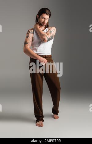Das ganze Barfußmodell ist ein stilvolles Modell mit einem Tattoo auf dem Körper, das auf Grau steht Stockfoto