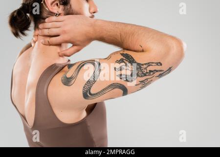 Schnittbild eines muskulösen Mannes im Tanktop, der den Hals berührt, isoliert auf grau Stockfoto
