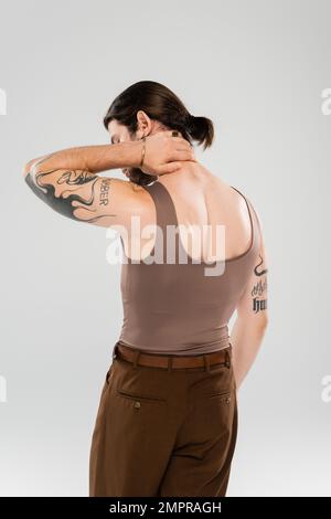 Seitenansicht eines muskulär tätowierten Mannes, der den Hals berührt, isoliert auf grau Stockfoto