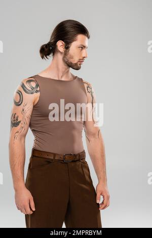 Seitenansicht eines tätowierten und langhaarigen Modells, das abseits auf Grau isoliert blickt Stockfoto