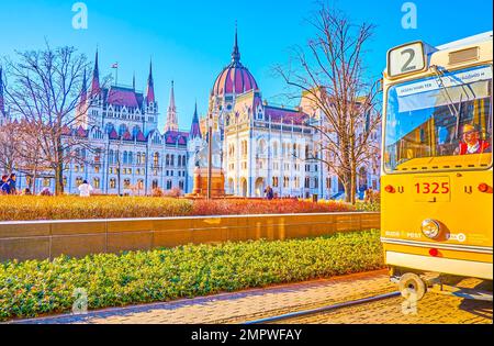 BUDAPEST, UNGARN - 2. MÄRZ 2022: Die traditionelle gelbe Straßenbahn von Budapest fährt auf dem Kossuth-Platz und passiert das Parlamentsgebäude am 2. März in Budapest Stockfoto