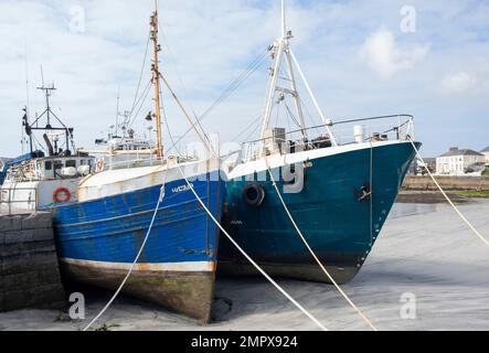 Zwei blaue Fischerboote entlang des Hafenkais in Irland, die bei Ebbe auf Sand im Hafen von Kilronan liegen, Inishmore Aran Islands County Galway Stockfoto