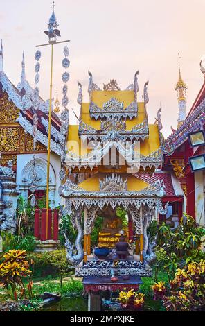 Der kleine Schrein mit kunstvoll verziertem Pyadendach und Buddha-Bild im Garten von Wat Mahawan, Chiang Mai, Thailand Stockfoto