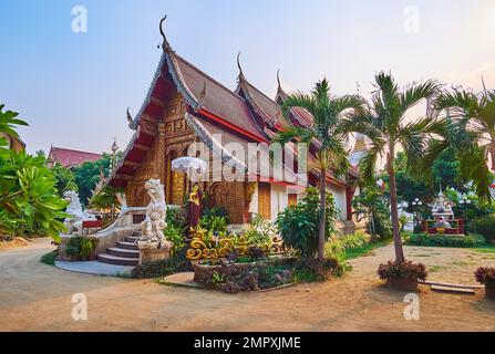Der tropische grüne Garten in Wat Mahawan mit mittelalterlichen Skulpturen von Viharn hinter den Palmen, Chiang Mai, Thailand Stockfoto