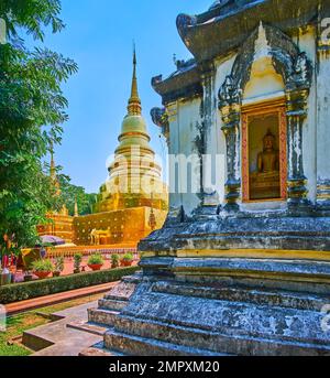 Der mittelalterliche weiße Kulai Chedi, dekoriert mit Buddha-Bild in einer Nische vor dem spektakulären goldenen Phra, den Luang Chedi auf dem Gelände von Wat Phra Singh Stockfoto