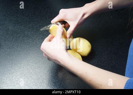 Eine Person, die nur mit den Händen sichtbar ist, schält Kartoffeln Stockfoto