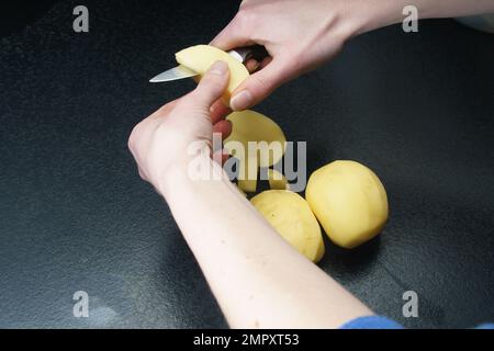 Eine Person, die nur mit den Händen sichtbar ist, schält Kartoffeln Stockfoto
