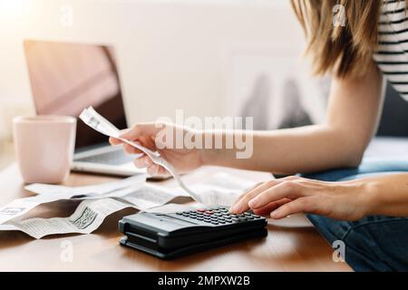 Junge Frau, die auf dem Sofa sitzt und den Taschenrechner zur Berechnung der Haushaltsausgaben verwendet Stockfoto