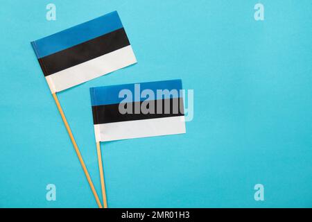Flache Lageansicht von zwei kleinen handgehaltenen estnischen Flaggen auf blauem Hintergrund mit viel Platz für Kopien. Stockfoto