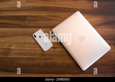 Weißrussland, Region Minsk - 17. März 2020: Apple Smartphone iPhone und Laptop liegen auf einem Schreibtisch aus Holz und sind gegen moderne Geräte. Stockfoto