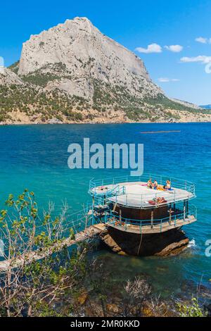 Novy Svit, Krim - 10. August 2020: Die Menschen ruhen sich an einem sonnigen Tag an der Schwarzmeerküste aus. Öffentlicher Strand von Novyi Svit, Gemeinde Sudak, Krim. Vertikal p Stockfoto