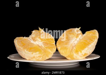 Zwei Hälften einer geschälten Orange auf einer weißen Keramikplatte, Makro, isoliert auf schwarzem Hintergrund. Stockfoto