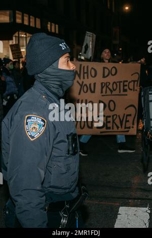 New York, Usa. 28. Januar 2023. Ein Polizist kommt an einem Plakat vorbei, auf dem steht: "Wem dienen Sie? Wen schützen Sie?“ Während des demonstrationsmarsches. Hunderte von Demonstranten gehen auf die Straßen von New York City als Reaktion auf das neu veröffentlichte Video, das die tödlichen Schläge von Tyre Nichols durch die Polizei von Memphis zeigt. Fünf Mitglieder der Memphis PD wurden anschließend gefeuert und wegen Mordes zweiten Grades angeklagt, aber die Demonstranten im ganzen Land sehen das Polizeisystem als jenseits der Erlösung. Kredit: SOPA Images Limited/Alamy Live News Stockfoto