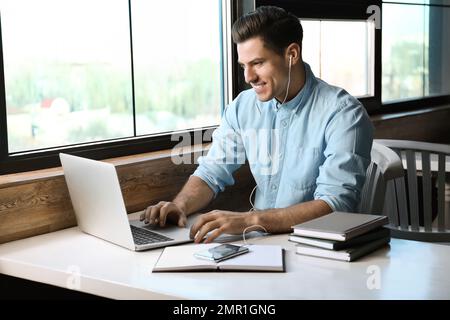 Ein Mann, der am Tisch im Café Hörbücher hört Stockfoto