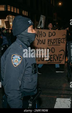 New York, Usa. 28. Januar 2023. Ein Polizist kommt an einem Plakat vorbei, auf dem steht: "Wem dienen Sie? Wen schützen Sie?“ Während des demonstrationsmarsches. Hunderte von Demonstranten gehen auf die Straßen von New York City als Reaktion auf das neu veröffentlichte Video, das die tödlichen Schläge von Tyre Nichols durch die Polizei von Memphis zeigt. Fünf Mitglieder der Memphis PD wurden anschließend gefeuert und wegen Mordes zweiten Grades angeklagt, aber die Demonstranten im ganzen Land sehen das Polizeisystem als jenseits der Erlösung. (Foto: Olga Fedorova/SOPA Images/Sipa USA) Guthaben: SIPA USA/Alamy Live News Stockfoto