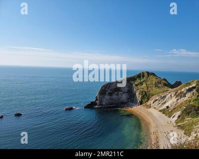 Durdle Door ist ein natürlicher Kalksteinbogen an der Jurassic Coast in der Nähe von Lulworth in Dorset. Der 120 Meter (390 Fuß) lange Isthmus, der den Kalkstein mit der Kreide verbindet, besteht aus einem 50 Meter (160 Fuß) langen Band aus Portlandkalkstein. Im Jahr 1811 nannte die erste Landkarte der Region die Region „Dirdale Door“. Durdle stammt aus dem alten englischen Durl, das heißt, durchbohren, bohren oder bohren, was wiederum von Thyrel abgeleitet wird, was Loch bedeutet. Der Teil des Namens Door behält wahrscheinlich seine moderne Bedeutung, die sich auf die Bogenform des Felsens bezieht; im späten 19. Jahrhundert wird er als „Ba“ bezeichnet Stockfoto