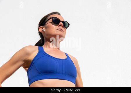 Nahaufnahme einer sportlichen Frau, die beim Training in der Sonne schnurlose Ohrhörer trägt Stockfoto