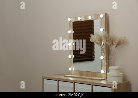Moderner Spiegel mit Lampen in der Nähe der beigefarbenen Wand im Zimmer Stockfoto