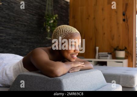 Glückliche afroamerikanische Frau, die ein Handtuch trug und auf dem Bett lag Stockfoto