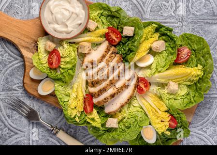 Essensfotografie mit caesar Salat mit gebratenem Hühnchen, Kopfsalat, Wachteleiern, Tomaten, Croutons, Soße Stockfoto