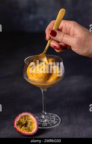 Lebensmittelfotografie von Passionsfrucht und Mangoeis, Sorbet, Chia, gefroren, kühl, Schaufel, Glas, Hand, Löffel Stockfoto