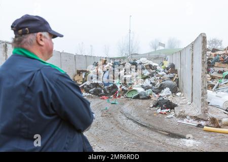 Ein Arbeiter im Recycling-Center, in dunkelblauer Arbeitskleidung, der sich einen unsortierten Müllhaufen ansieht, ist gerade in der Materialrückgewinnungsanlage angekommen, Rückansicht. Stockfoto