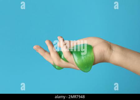 Frau spielt mit grünem Schleim auf hellblauem Hintergrund, Nahaufnahme. Anti-Stress-Spielzeug Stockfoto