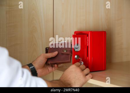 Ein Mann, der Brieftasche in einen kleinen Safe aus rotem Stahl steckt Stockfoto