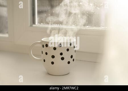 Eine Tasse heißes Getränk in der Nähe des Fensters an Regentagen Stockfoto