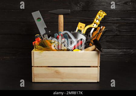 Holzkiste mit verschiedenen Zimmermannswerkzeugen auf schwarzem Tisch Stockfoto