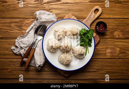 Khinkali, traditionelles Gericht der georgischen kaukasischen Küche, Teigtaschen gefüllt mit Hackfleisch auf weißem Teller mit Kräutern auf rustikalem Holztisch Stockfoto