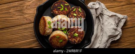 Hausgemachte Schnitzel aus Fisch, Hühnchen oder Fleisch auf schwarzer Gusseisenpfanne Pfannkuchen auf rustikalem Holztisch, traditionell geröstete gesunde Schnitzel in Stockfoto