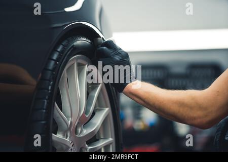 Schwärzung des Reifenrads mit einem Schwamm. Verfahren zur Detaillierung von Fahrzeugen. Nahaufnahme im Innenbereich. Nicht erkennbarer Facharzt während der Arbeit. Hochwertiges Foto Stockfoto