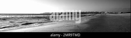 Panoramablick auf einen Sandstrand und eine ferne Skyline der Stadt. Schwarzweißfotografie. Stockfoto