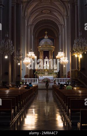 Eine vertikale Aufnahme des wunderschönen Inneren einer katholischen Kirche mit Menschen, die auf Bänken sitzen Stockfoto