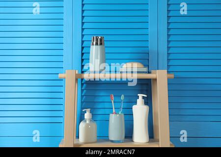 Hölzerne Regale mit Toilettenartikeln in der Nähe der blauen Klappwand. Innenelement des Badezimmers Stockfoto