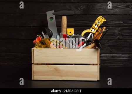 Holzkiste mit verschiedenen Zimmermannswerkzeugen auf schwarzem Tisch Stockfoto