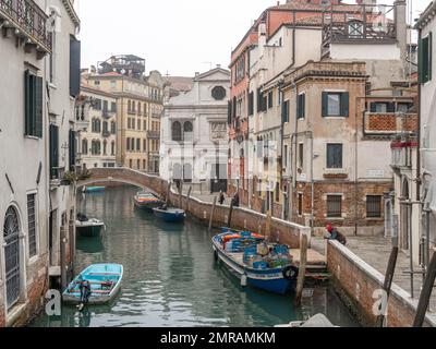 Grachtszene in Venedig mit einem kleinen Boot in einer ruhigen Wohngegend von Venedig im Winter an einem kühlen nebligen Tag mit ein paar Leuten auf der Straße Stockfoto