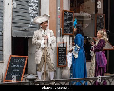 Menschen in mittelalterlichen Karnevalskostümen - ein Mann spricht mit zwei Frauen vor dem geschlossenen Café mit Outdoor-Menü in den Straßen von Venedig, Italien, Dura Stockfoto