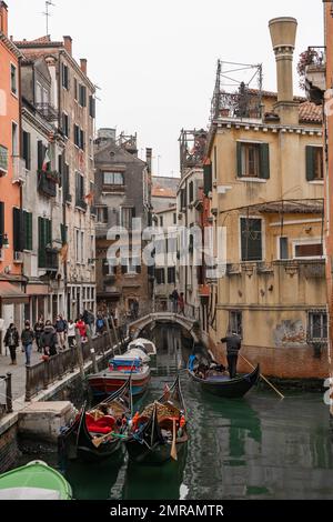 Venedig Kanalszene mit kleinen Booten und Gondeln in einem Wohngebiet von Venedig im Winter an einem kühlen grauen Tag mit einem Menschen auf der Straße Stockfoto