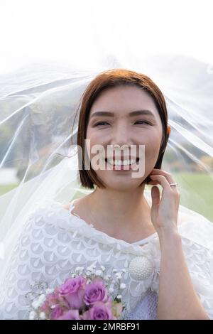 Vertikales Porträt einer lächelnden asiatischen Braut mit Schleier bei einer Hochzeit im Freien, Kopierbereich Stockfoto