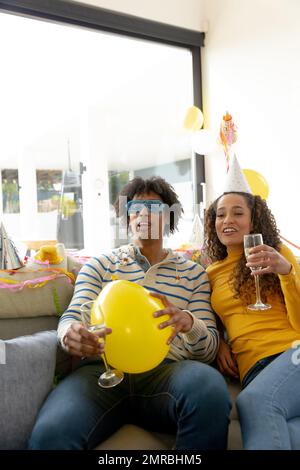 Ein glückliches birassisches Paar, das feiert, auf der Couch sitzt und Champagner trinkt, Kopierraum Stockfoto