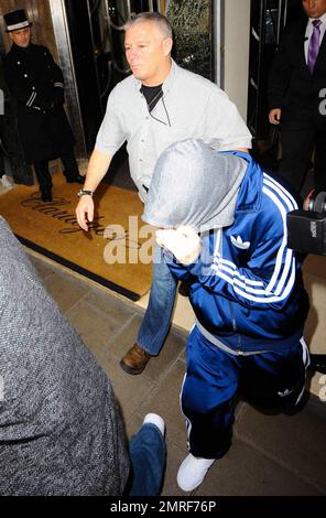 Der Teenager-Pop-Superstar Justin Bieber bedeckt Kopf und Gesicht mit einem grauen Kapuzenpullover, während er aus seinem Luxushotel in einer riesigen Menge von Fans und Fotografen rausgeeilt ist. In einem blauen Adidas-Trainingsanzug tat Bieber sein Bestes, um unauffällig zu bleiben, da er von Bodyguards und Sicherheitskräften zu einem wartenden Fahrzeug geführt wurde. London, Großbritannien. 3/17/11. Stockfoto