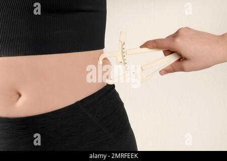 Ernährungswissenschaftler misst die Körperfettschicht der Frau mit einem Messschieber auf beigem Hintergrund, Nahaufnahme Stockfoto