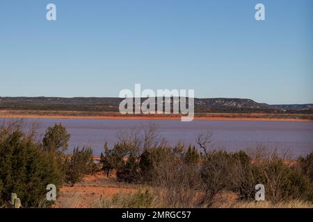 Lake Abilene ein Reservoir im Texas Hill Country, während die rote Sandküste das Wasser rosa und rot färbt. Stockfoto