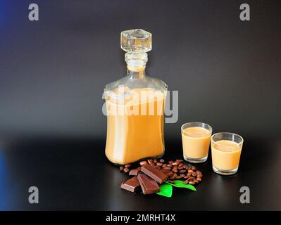 Traditioneller irischer Likör in einer Flasche und zwei Gläsern auf schwarzem Hintergrund, neben Schokoladenstückchen, Minzblättern und gerösteten Kaffeebohnen. Stockfoto