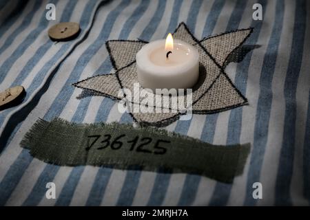 Brennende Kerze, jüdische Marke und Nummer auf der Uniform, Nahaufnahme. Internationaler Holocaust-Gedenktag Stockfoto