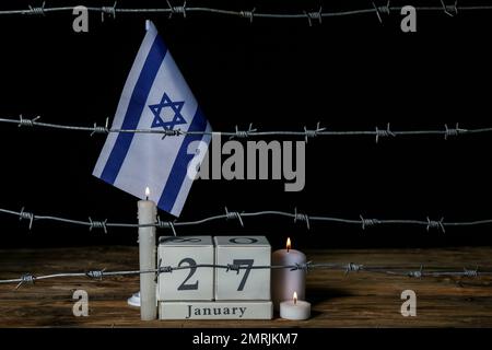 Kalender mit Datum 27. JANUAR, brennenden Kerzen, Stacheldraht und Flagge Israels auf dem Tisch. Internationaler Holocaust-Gedenktag Stockfoto