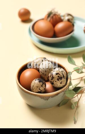 Teller und Schüssel mit Ostereiern auf gelbem Hintergrund Stockfoto