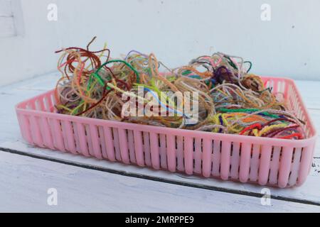 Ein Haufen übrig gebliebenes farbenfrohes Wollgarn in einem rosafarbenen Kunststoffbehälter auf dem Tisch Stockfoto